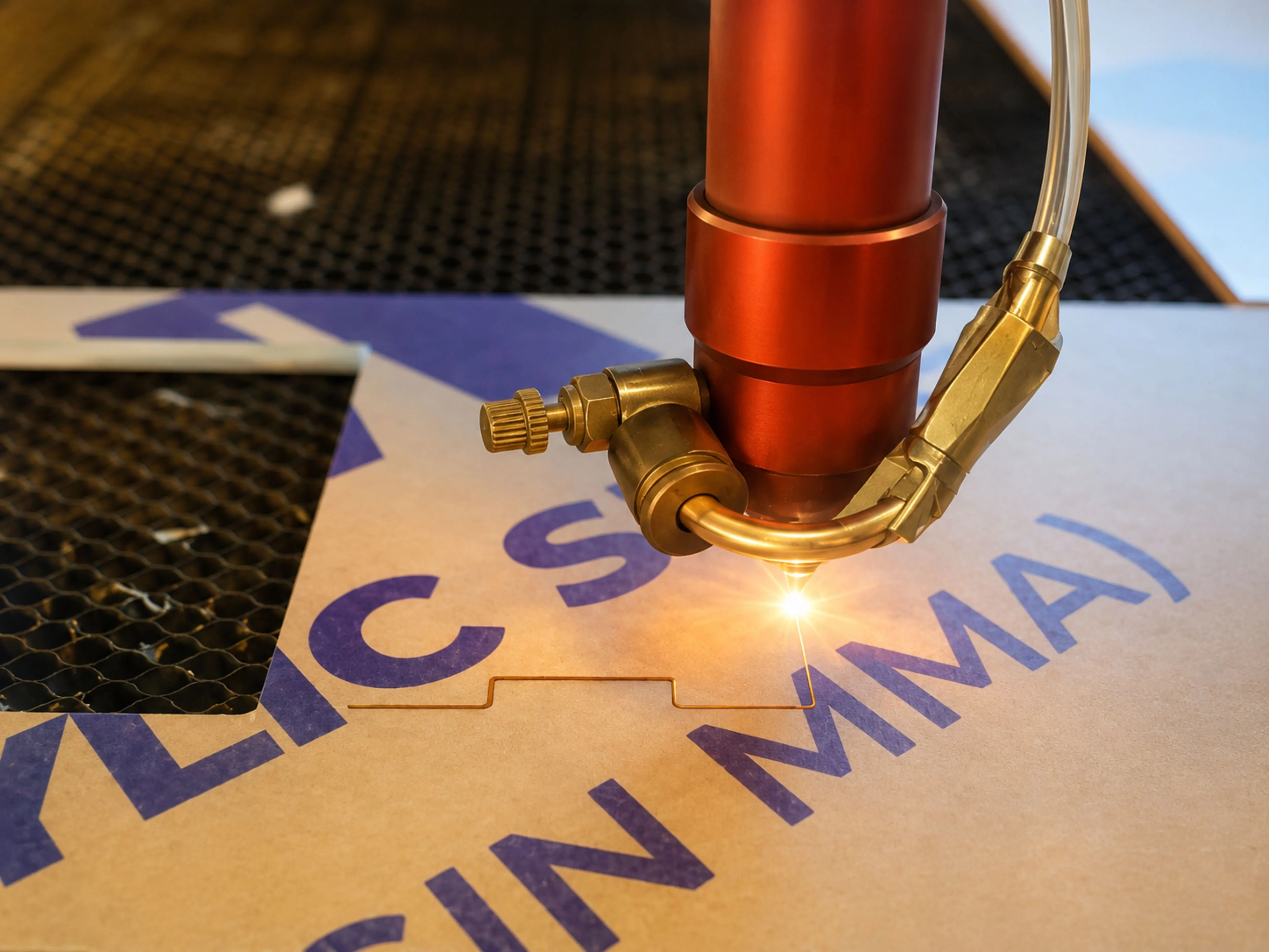CO2 laser head mid-cut on a sheet of cast acrylic, honeycomb bed visible