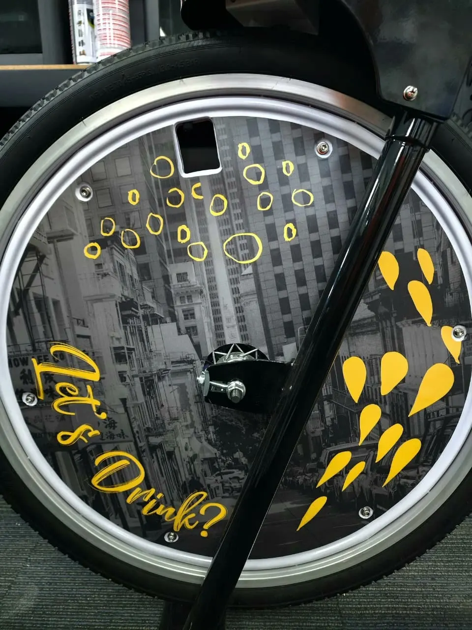 Close-up of the StrEat Culture wheel disc: grey city street, gold bubbles and drops, Let's Drink? in gold script