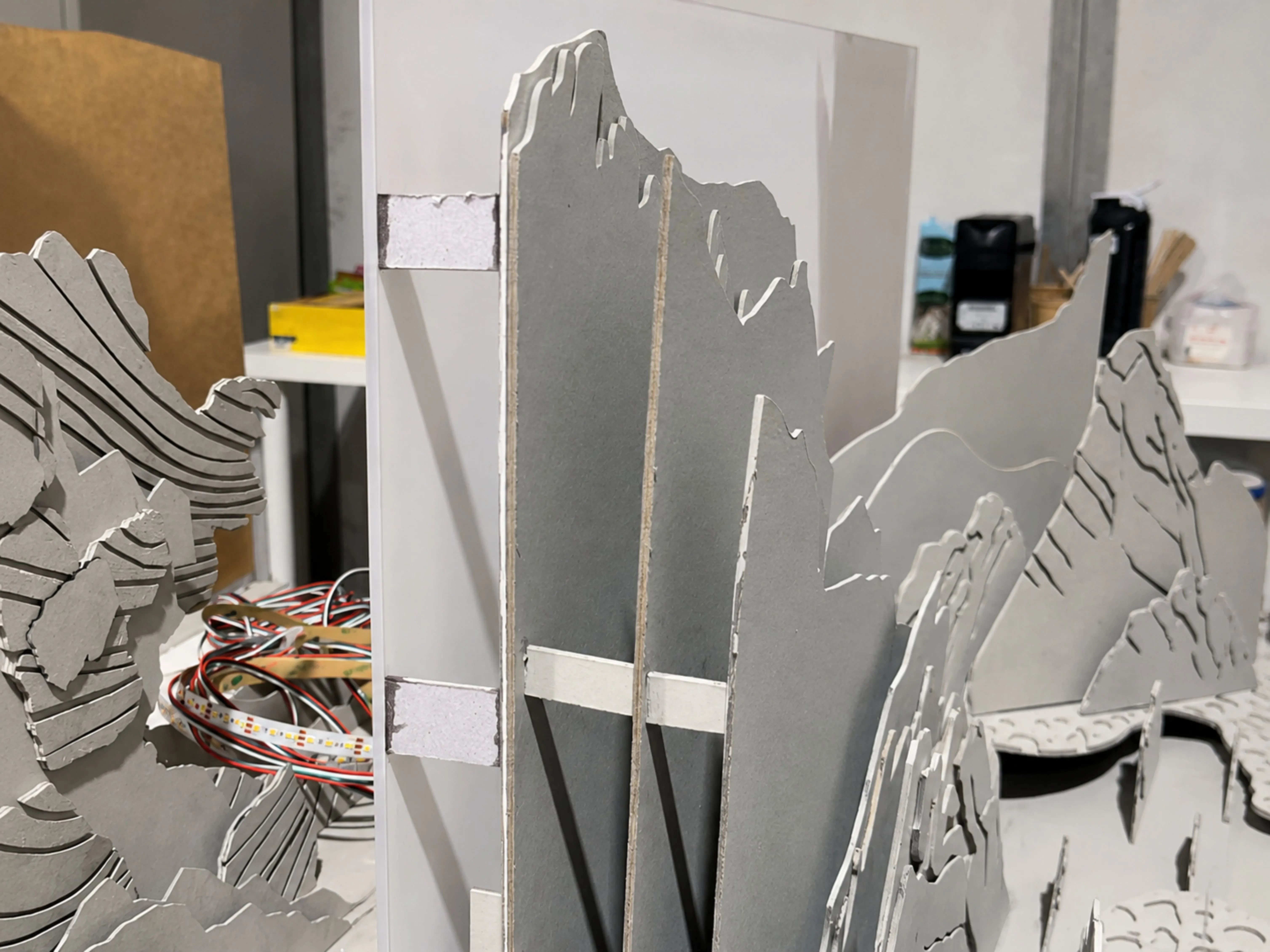 Layered grey-board cliff cutouts being assembled on the workshop bench with LED strips routed in